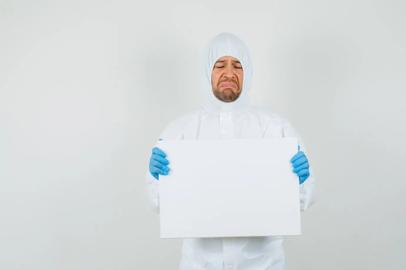 Мужчина-врач в защитном костюме держит пустой холст.