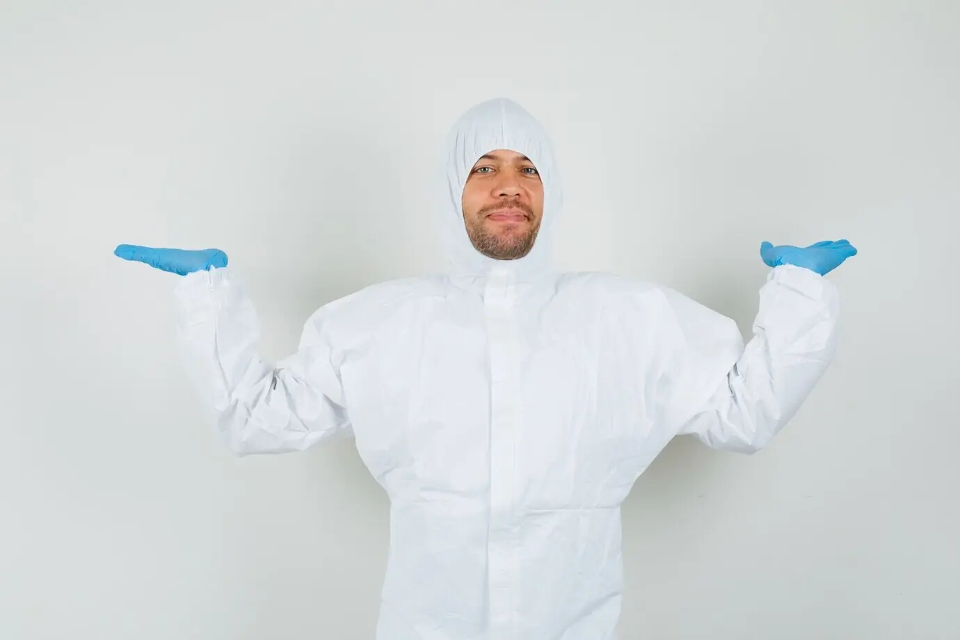 Врач-мужчина в защитном костюме делает жест весов.